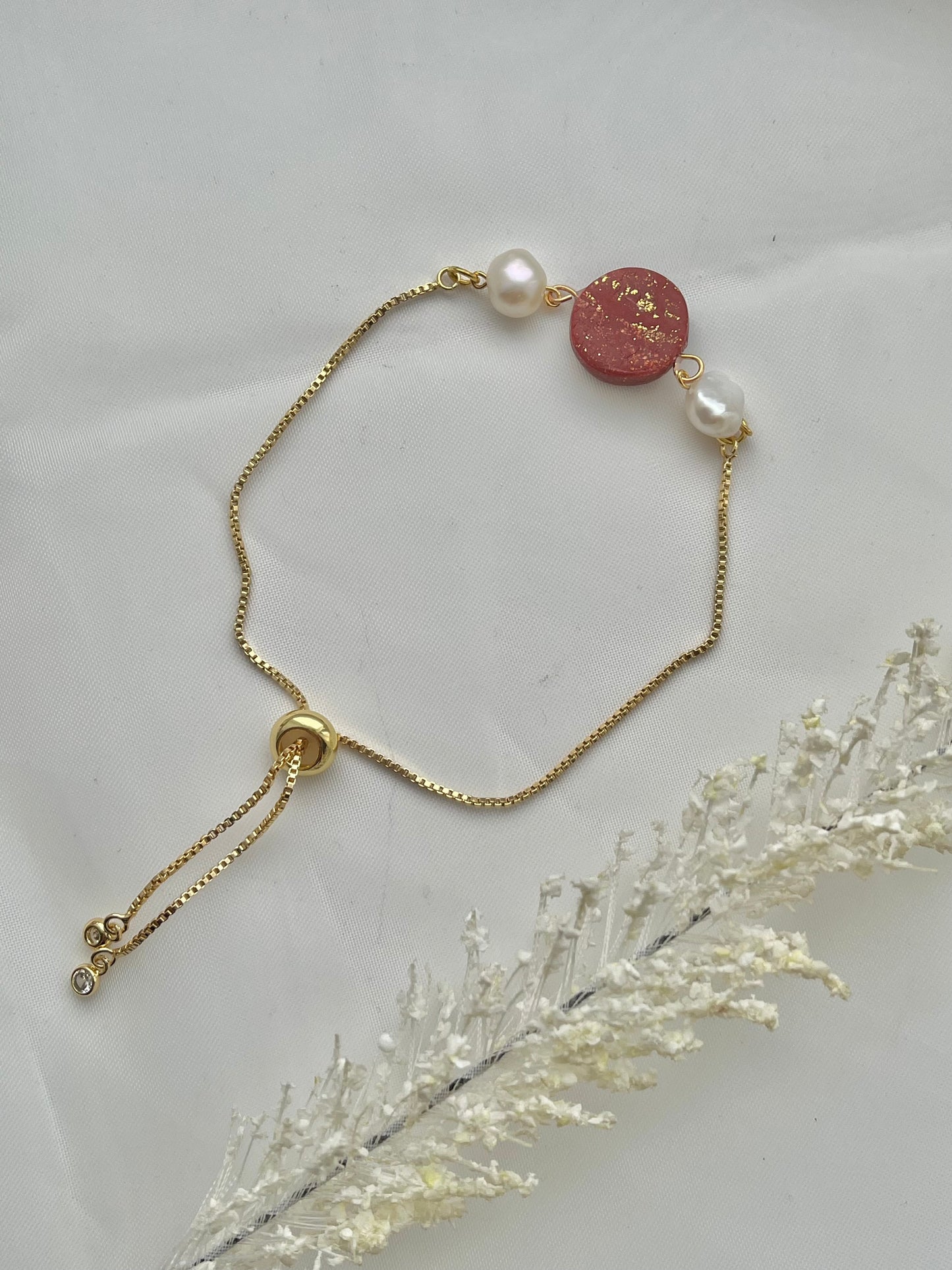 A bracelet with a dark red clay circle with freshwater pearls on either side laid flat down to show the adjustable slider