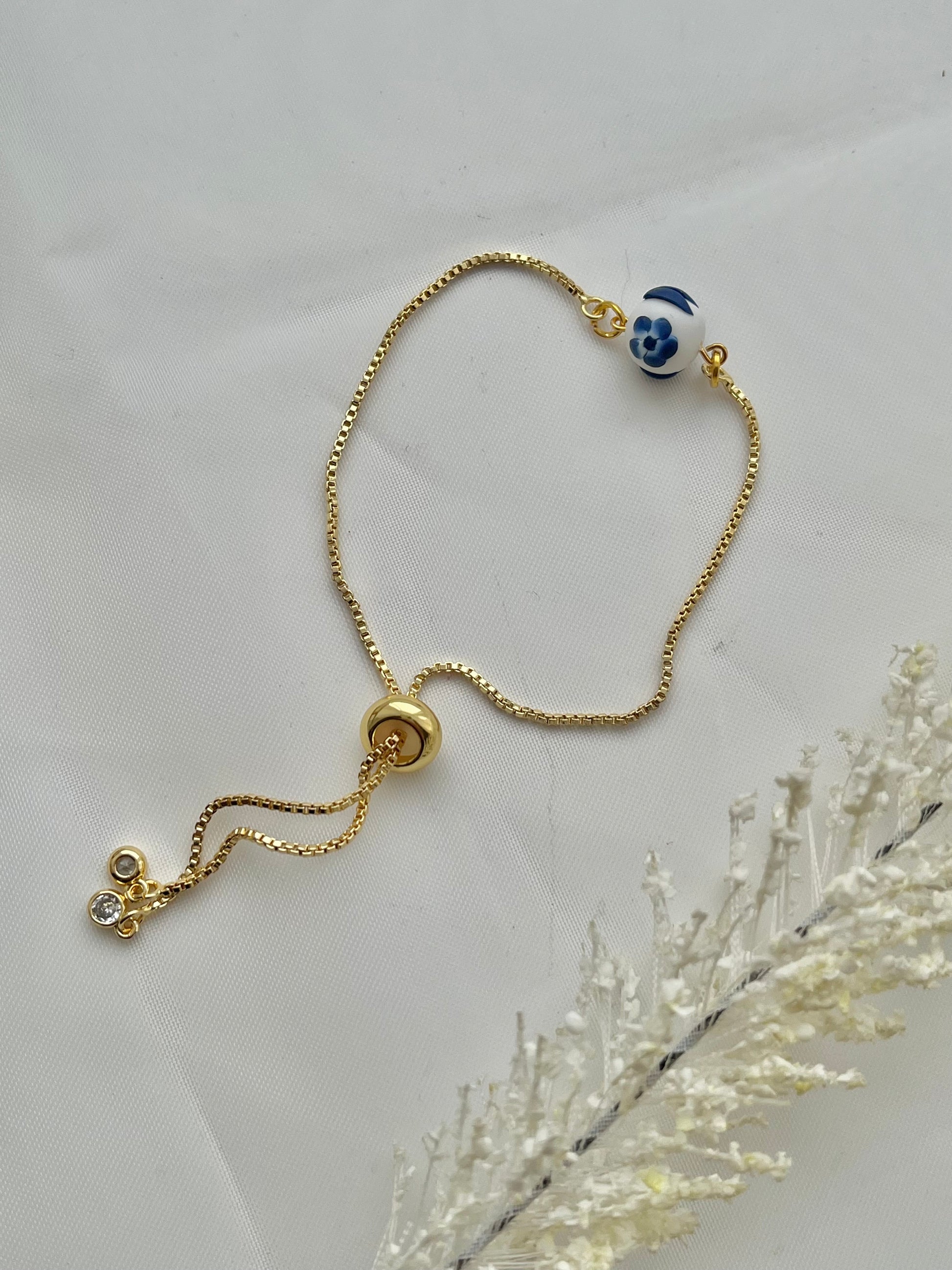 A floral bracelet in blue and white china pottery style with 1 beads laid down flat to show adjustable slider on the bracelet