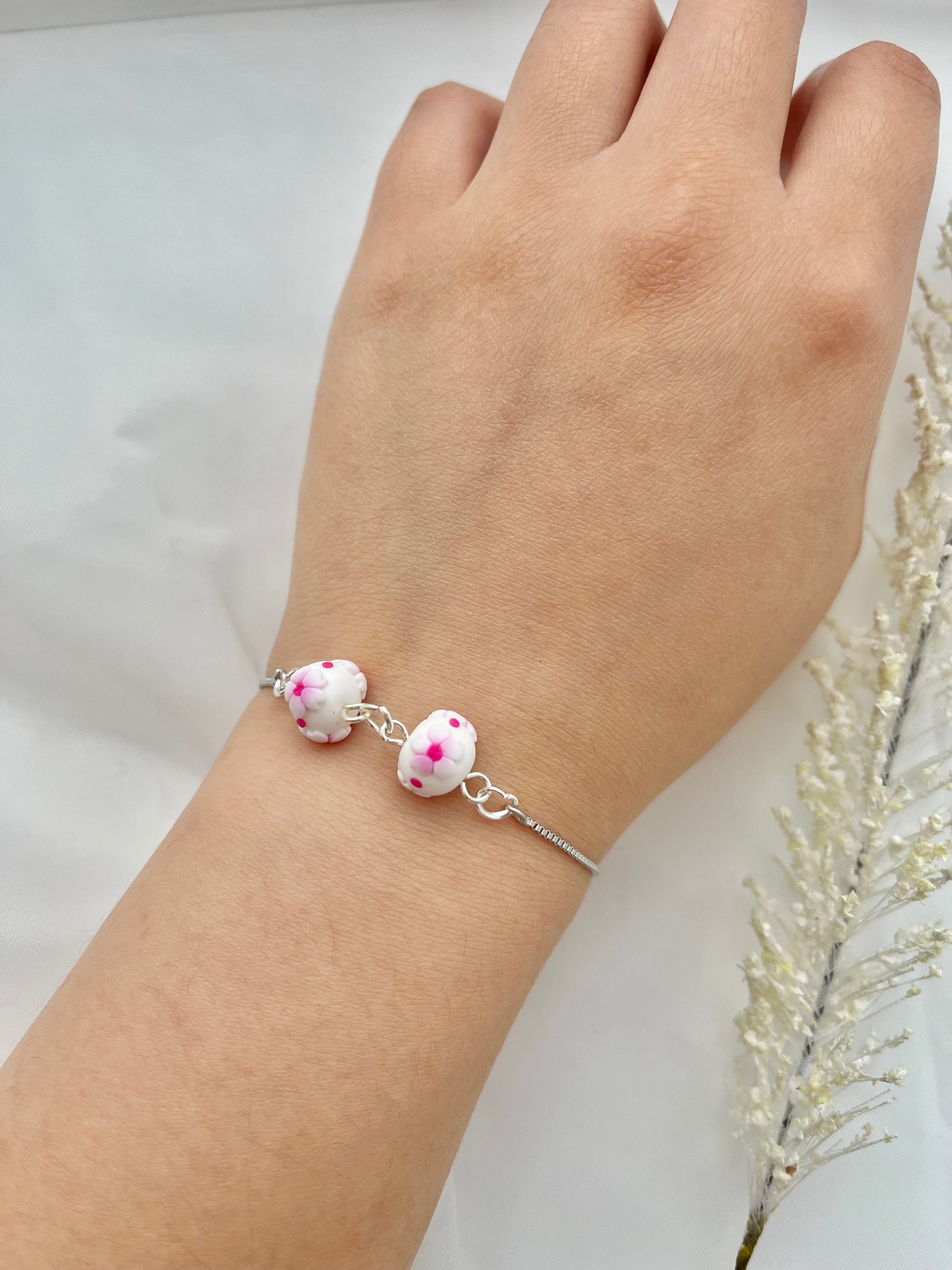 A floral bracelet with a rhodium plated chain in cherry blossom style with 2 beads on a hand