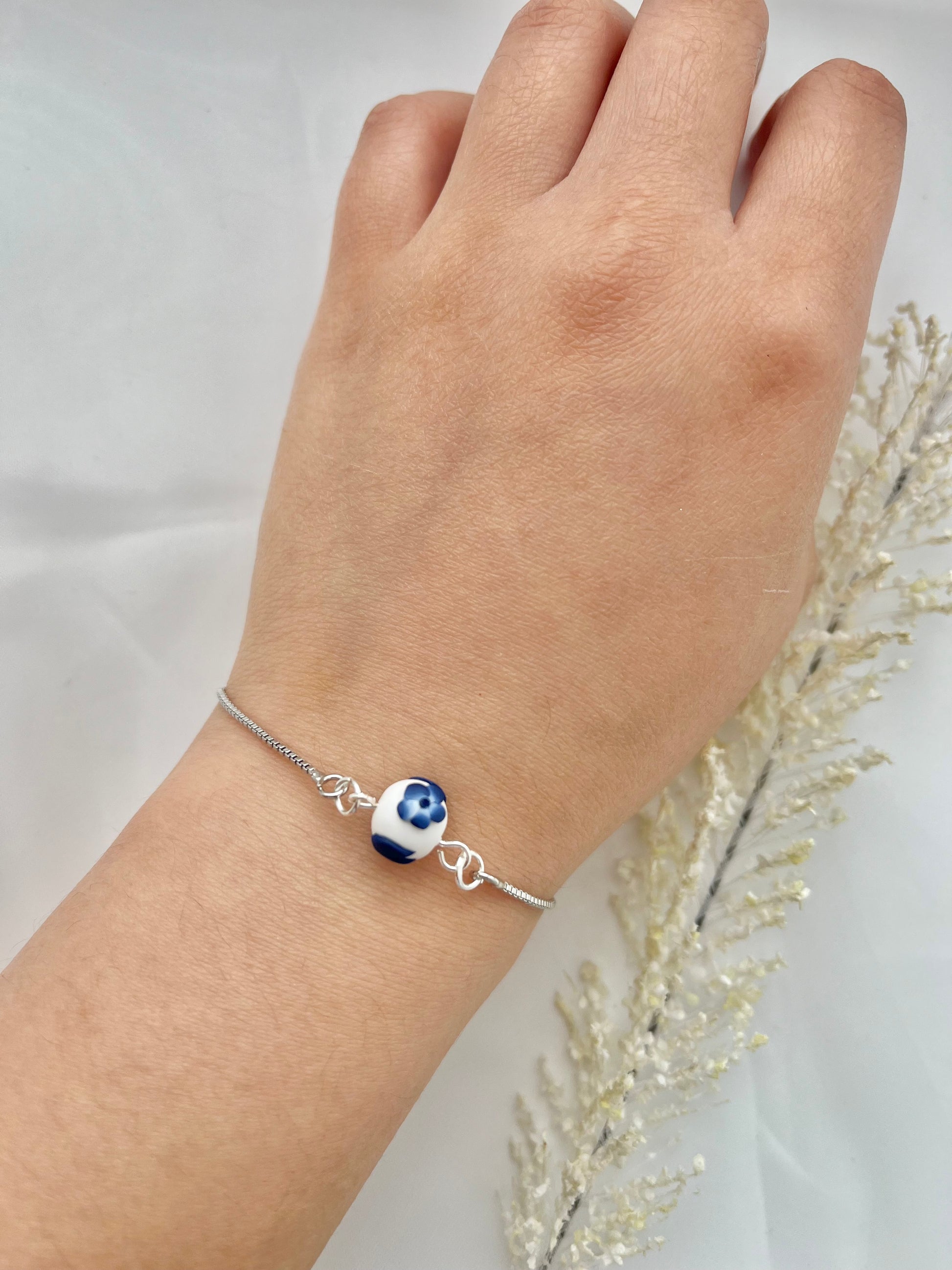 A floral bracelet with rhodium plated chain in blue and white china pottery style with 1 bead on a hand
