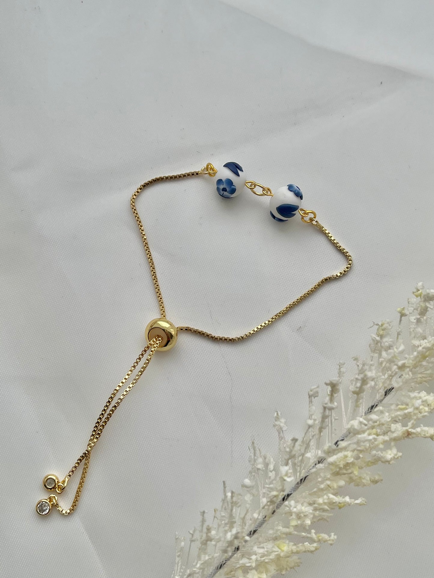 A floral bracelet in blue and white china pottery style with 2 beads laid down flat to show adjustable slider on the bracelet