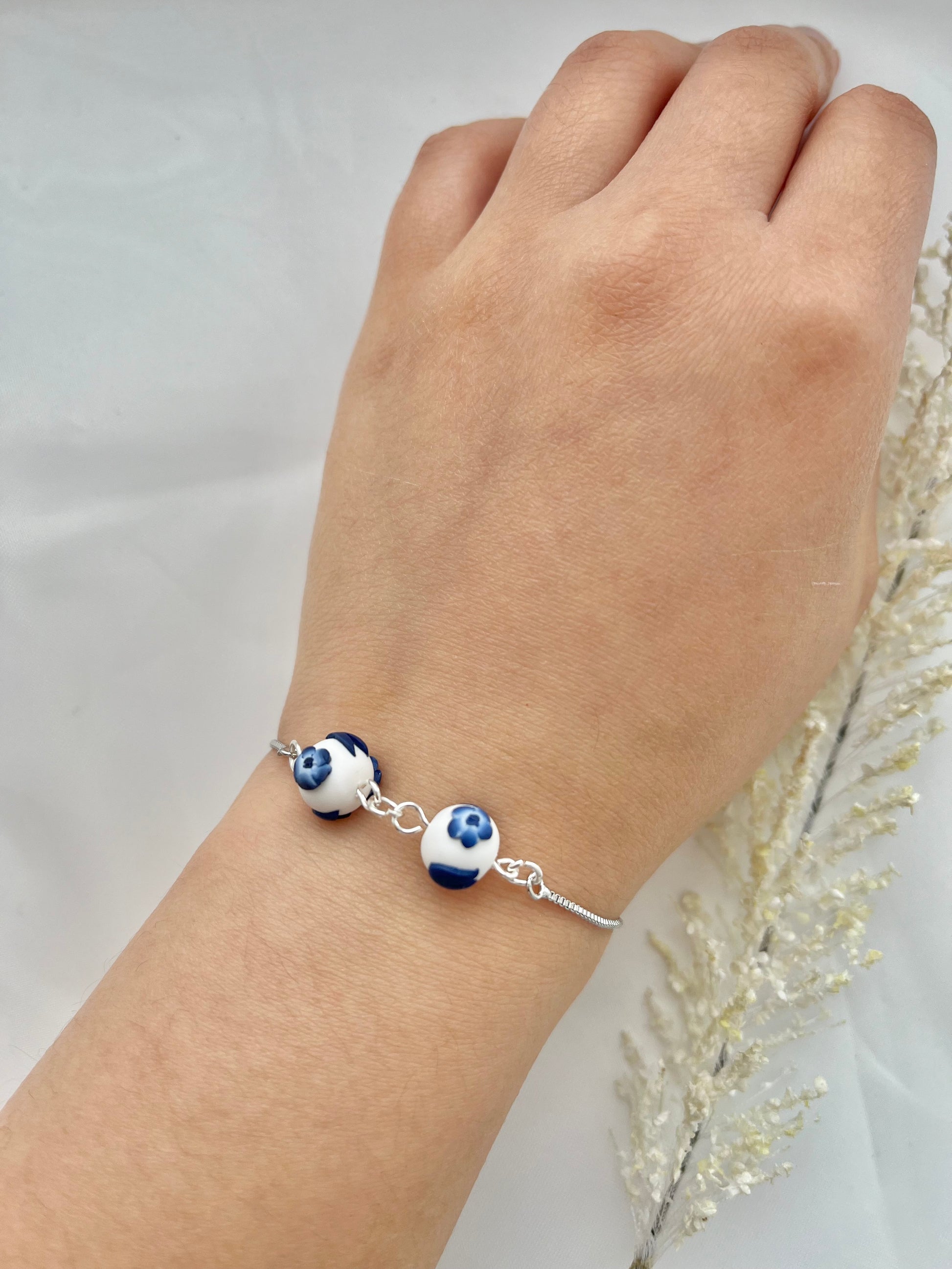 A floral bracelet with rhodium plated chain in blue and white china pottery style with 2 beads on a hand