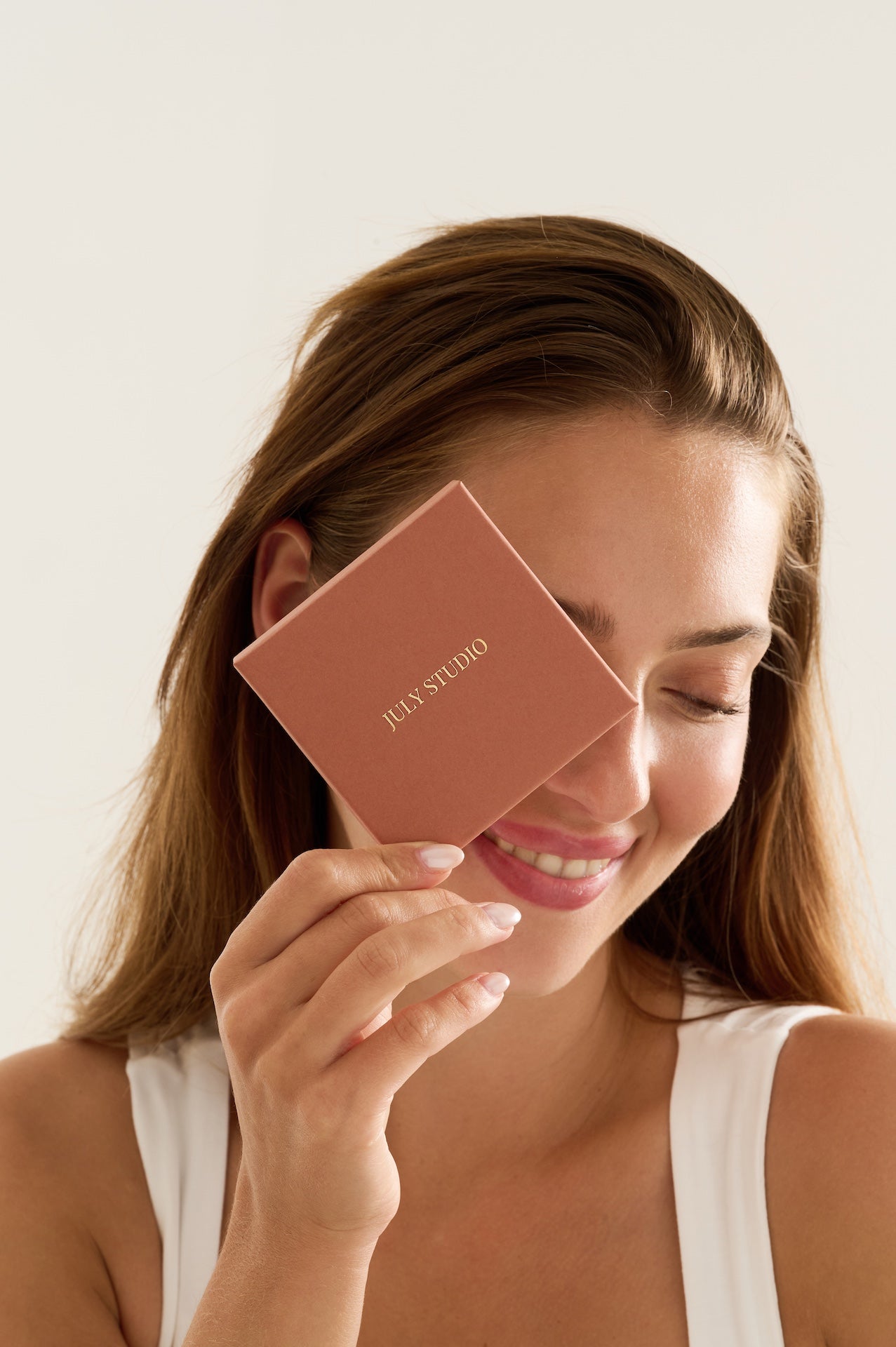 Smiling woman holding a July Studio jewellery box against a white background