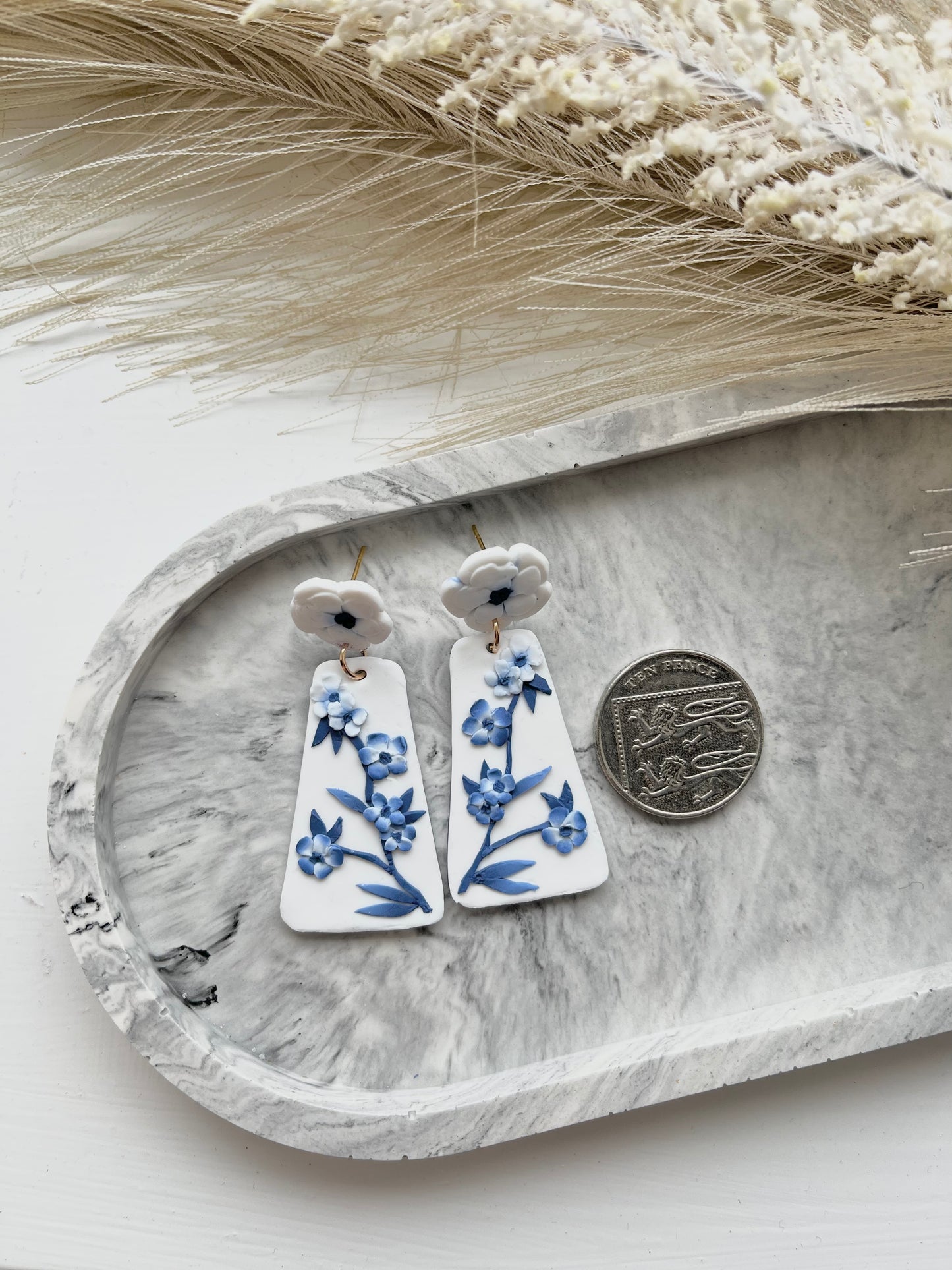 Long blue and white floral blue china clay earrings on a grey trinket dish, with a 10p coin showing relative size