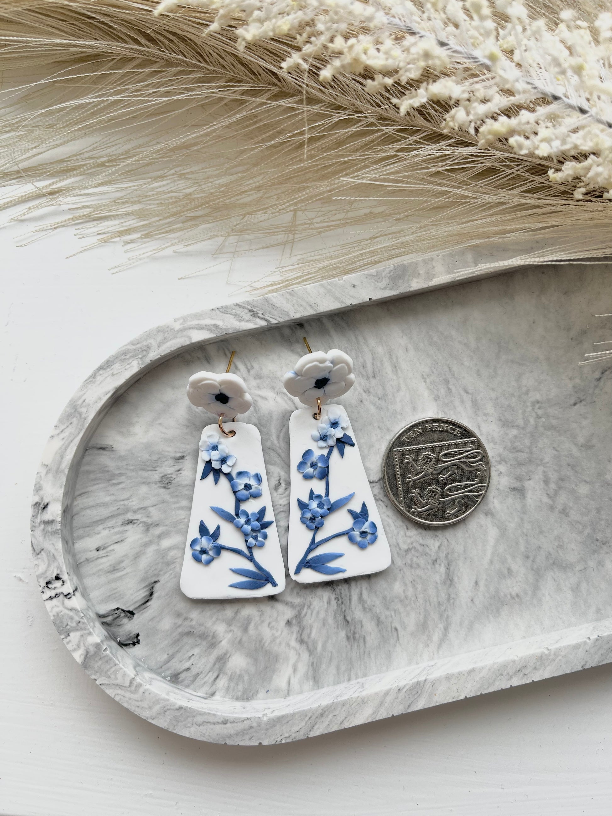 Long blue and white floral blue china clay earrings on a grey trinket dish, with a 10p coin showing relative size