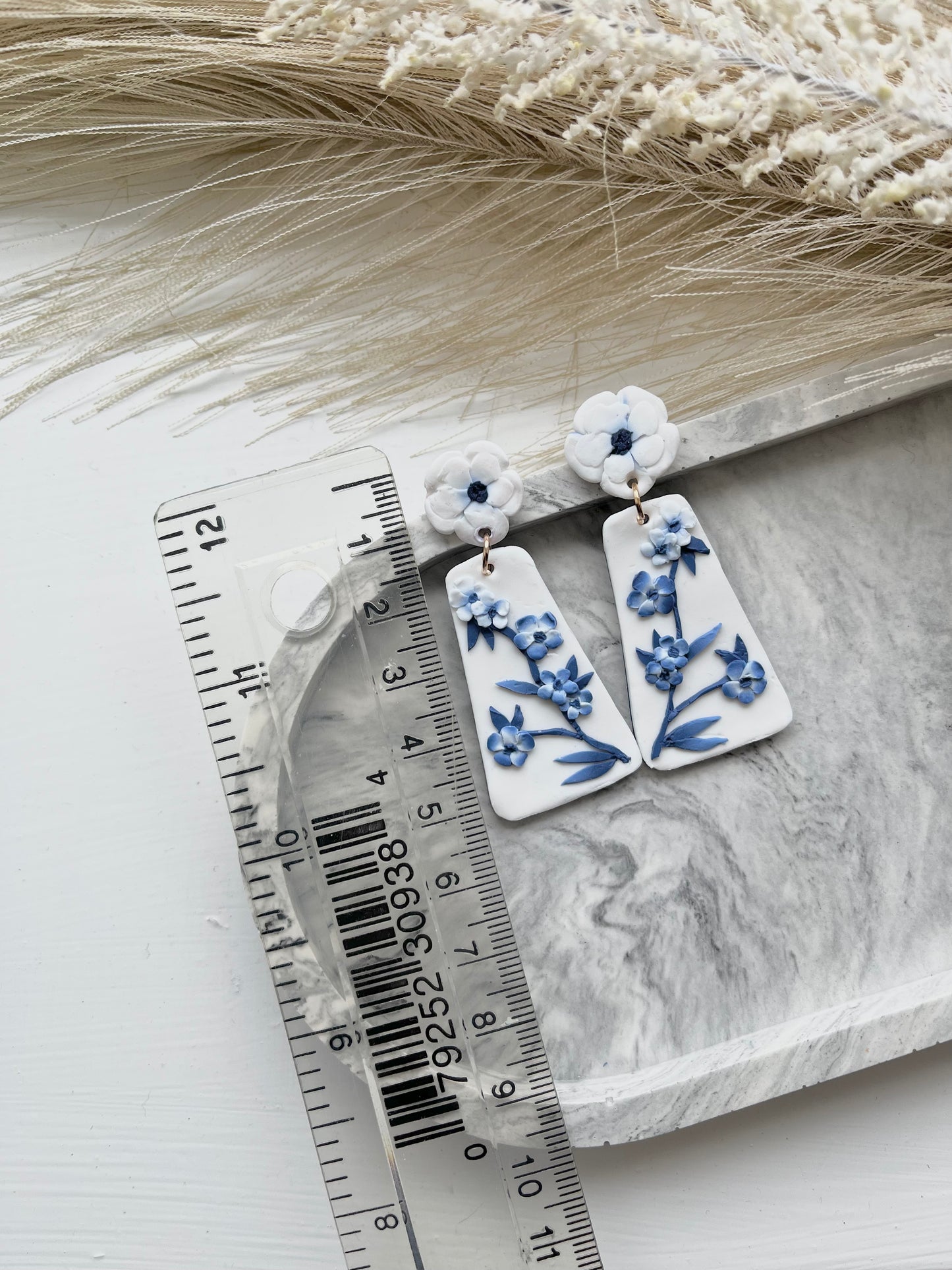Long blue and white floral blue china clay earrings on a grey trinket dish, with a ruler showing dimensions