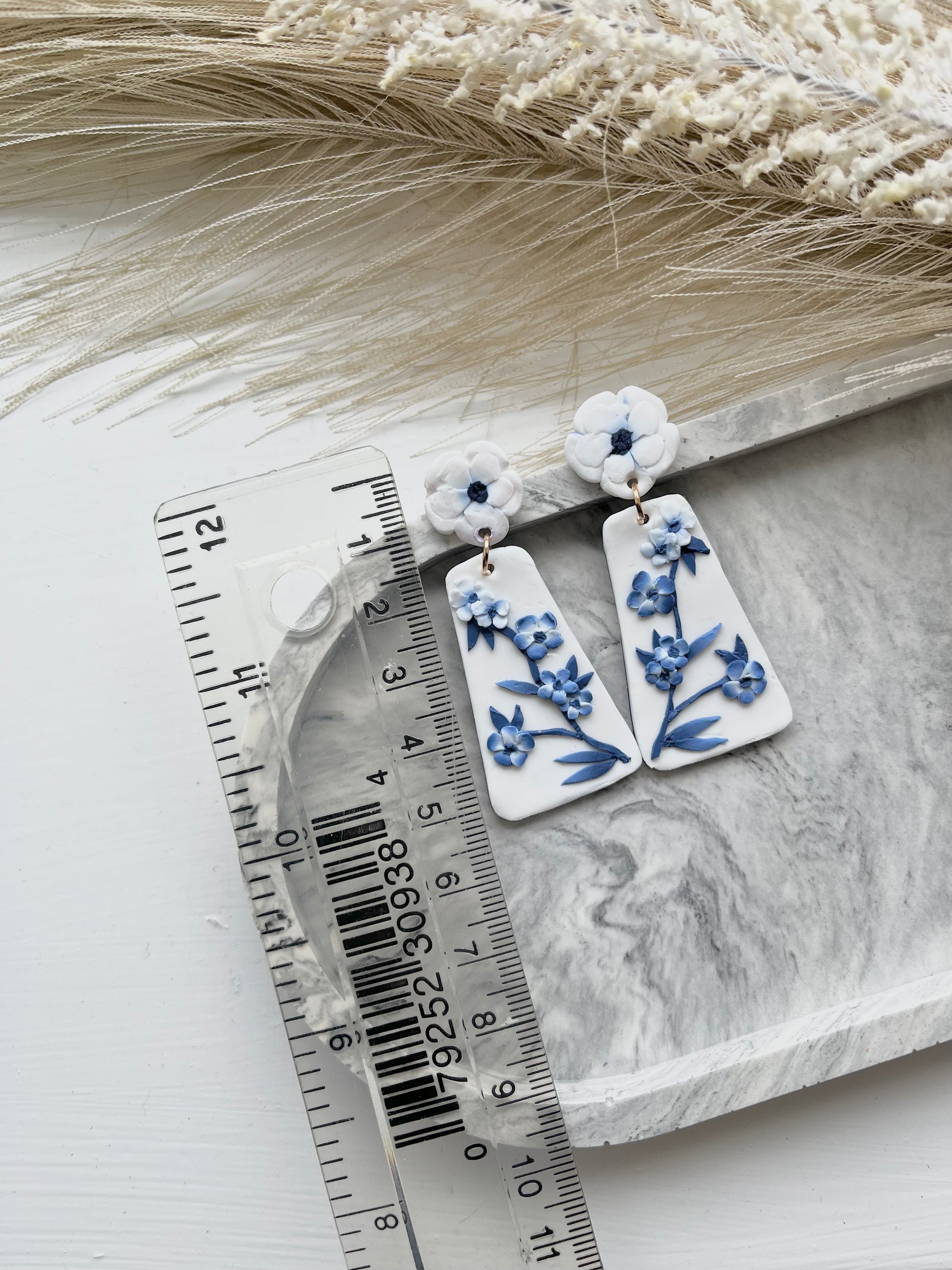 Long blue and white floral blue china clay earrings on a grey trinket dish, with a ruler showing dimensions