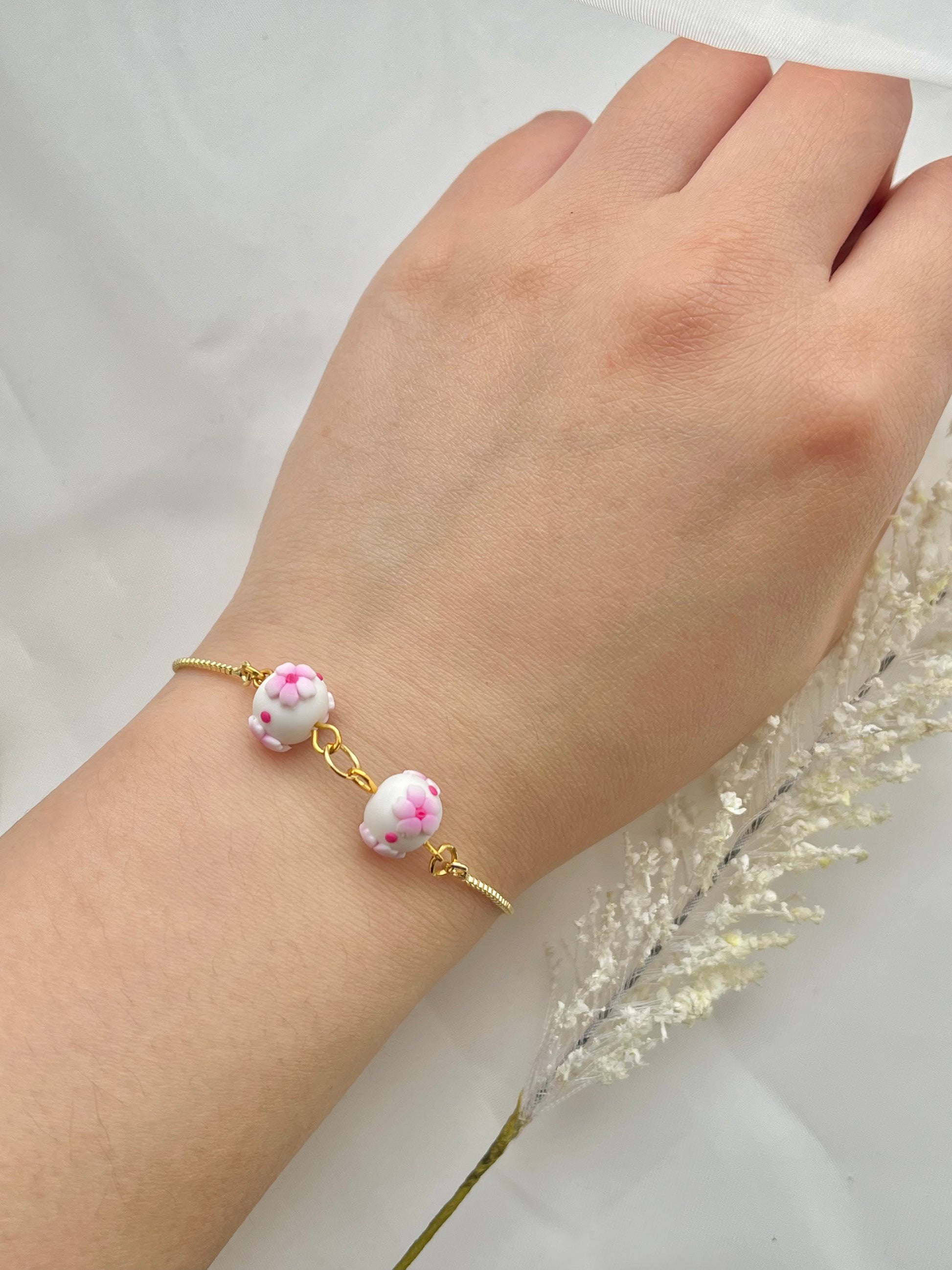A floral bracelet in cherry blossom style with 2 beads on a hand
