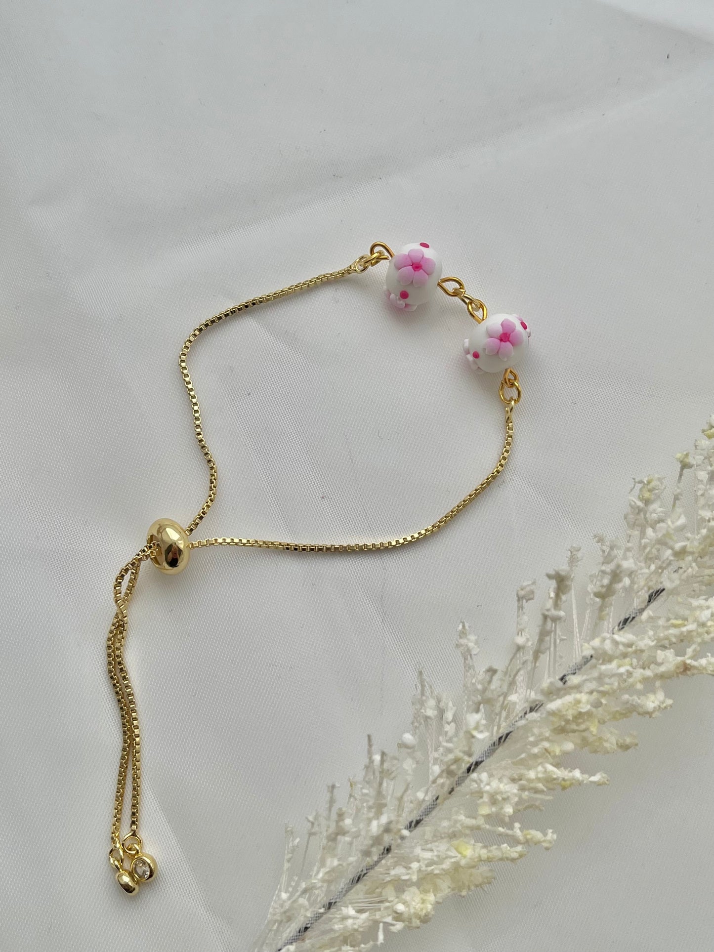A floral bracelet in cherry blossom style laid flat to show the adjustable slider