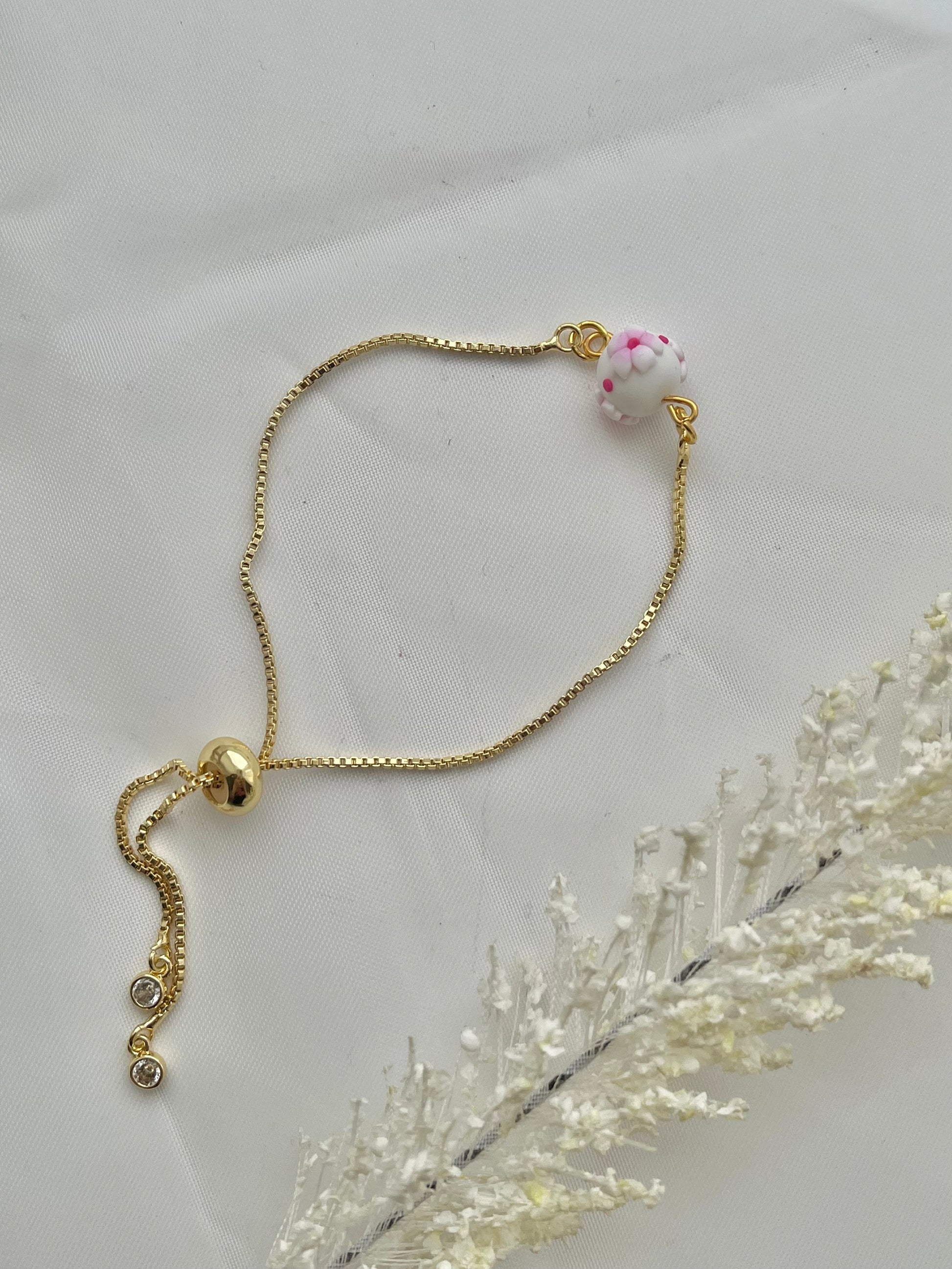 A floral bracelet in cherry blossom style with 1 bead laid flat down to show the adjustable slider