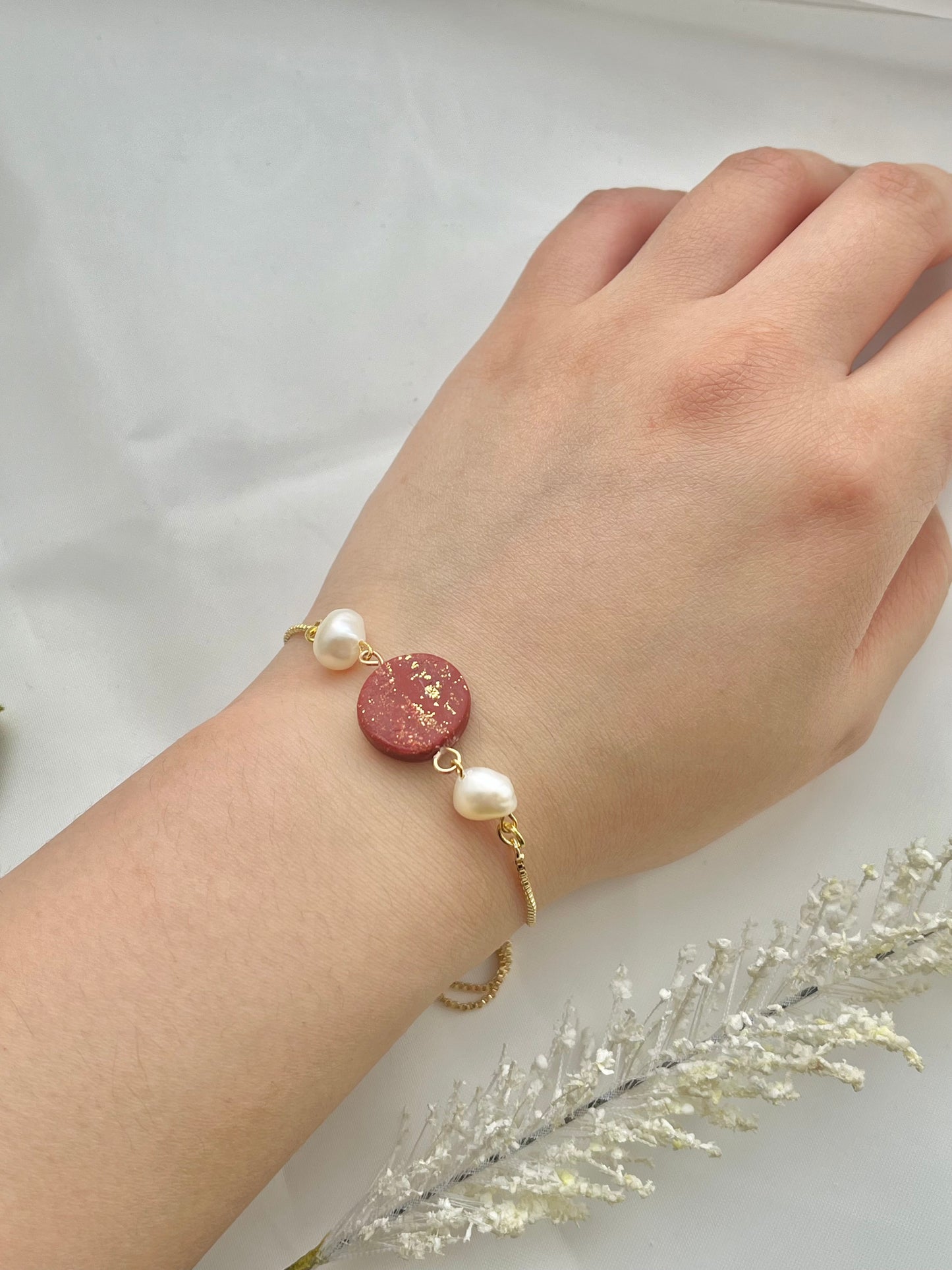 A bracelet with a dark red clay circle with freshwater pearls on either side on a hand
