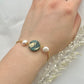 A bracelet with a dark green clay circle with freshwater pearls on either side on a hand
