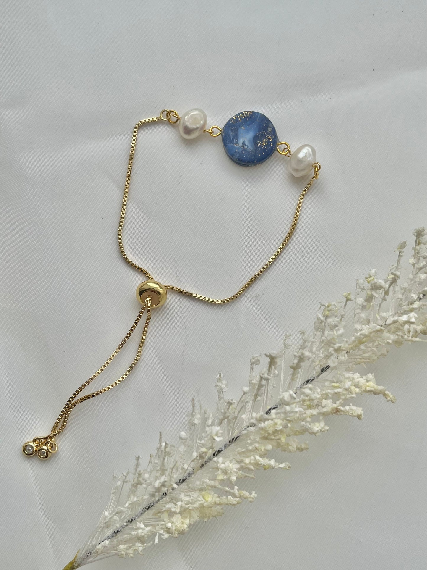 A bracelet with a dark blue clay circle with freshwater pearls on either side laid flat down to show the adjustable slider