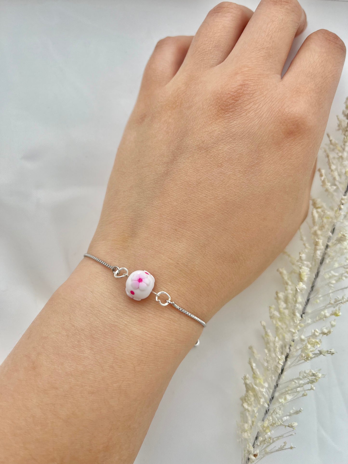 A floral bracelet with a rhodium plated chain in cherry blossom style with 1 bead on a hand