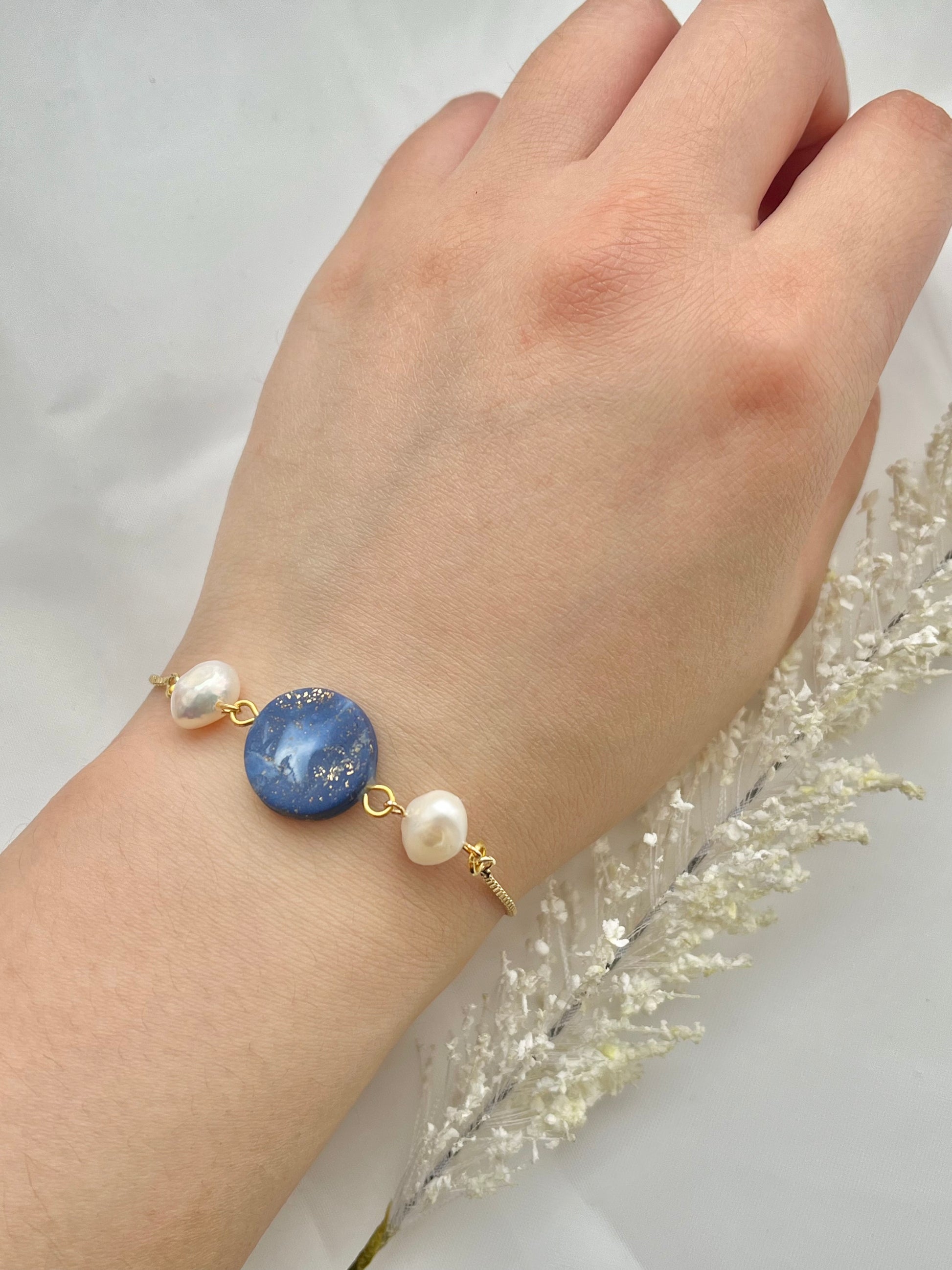 A bracelet with a dark blue clay circle with freshwater pearls on either side on a hand