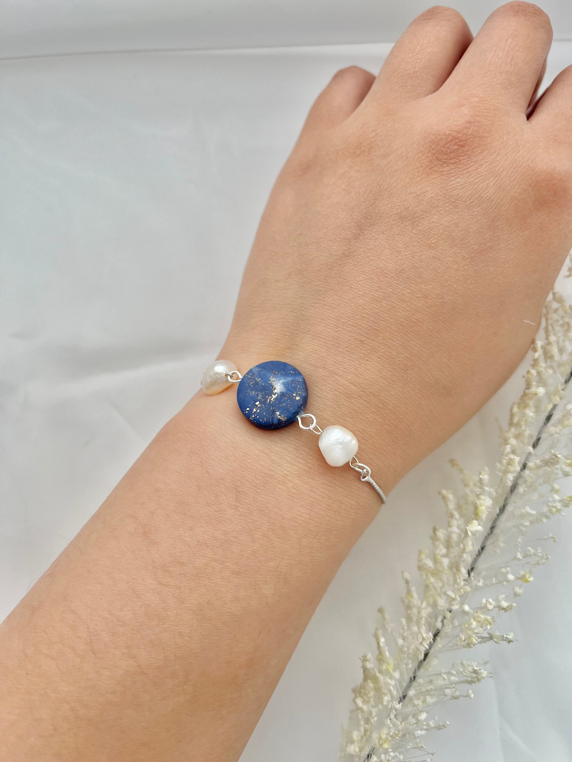 A rhodium plated bracelet with a dark blue clay circle with freshwater pearls on either side on a hand
