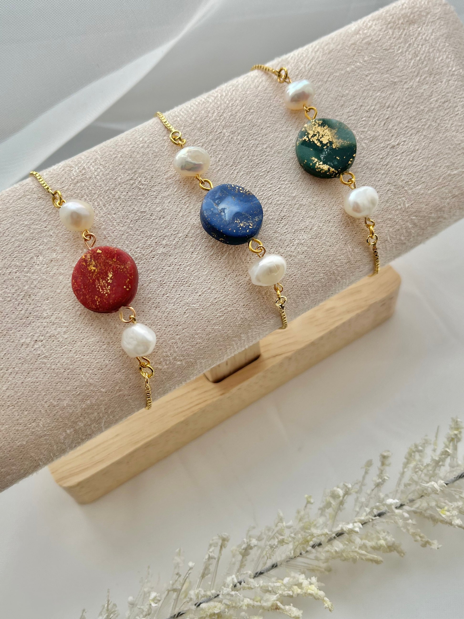 Three bracelets with a clay centre and 2 freshwater pearls either side. Pictured in dark red, dark blue and dark green.