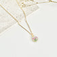 A gold clay necklace with a small carnation pendant laid on a flat white surface next to dried flowers