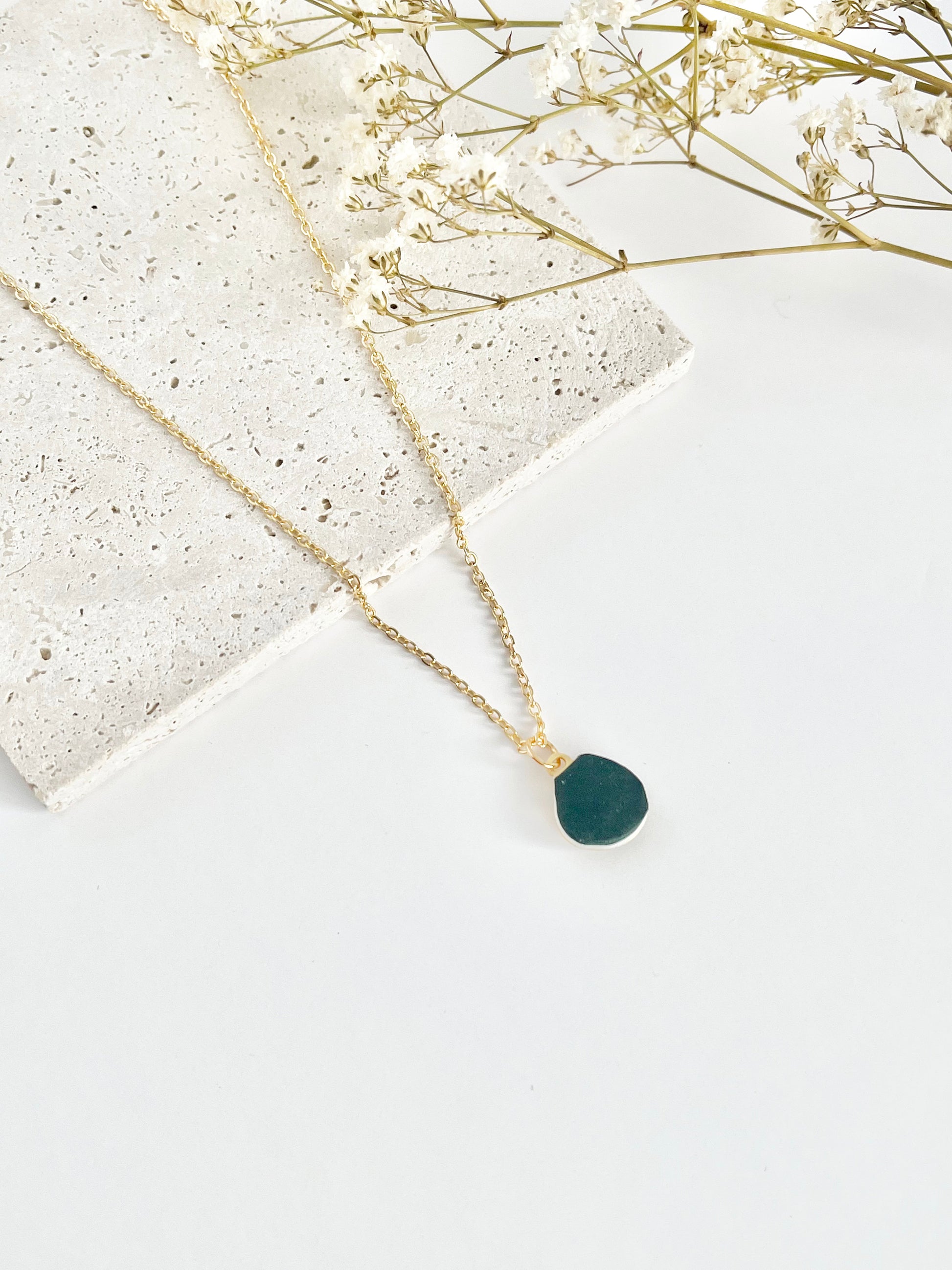 Gold clay necklace with a green pendant on a light background