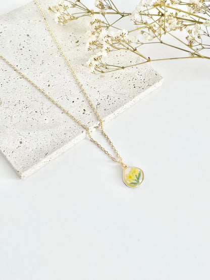 Gold clay necklace with a small daffodil pendant on a white surface with dried flowers.