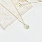 Gold clay necklace with a lily of the valley pendant on a white surface with dried flowers.