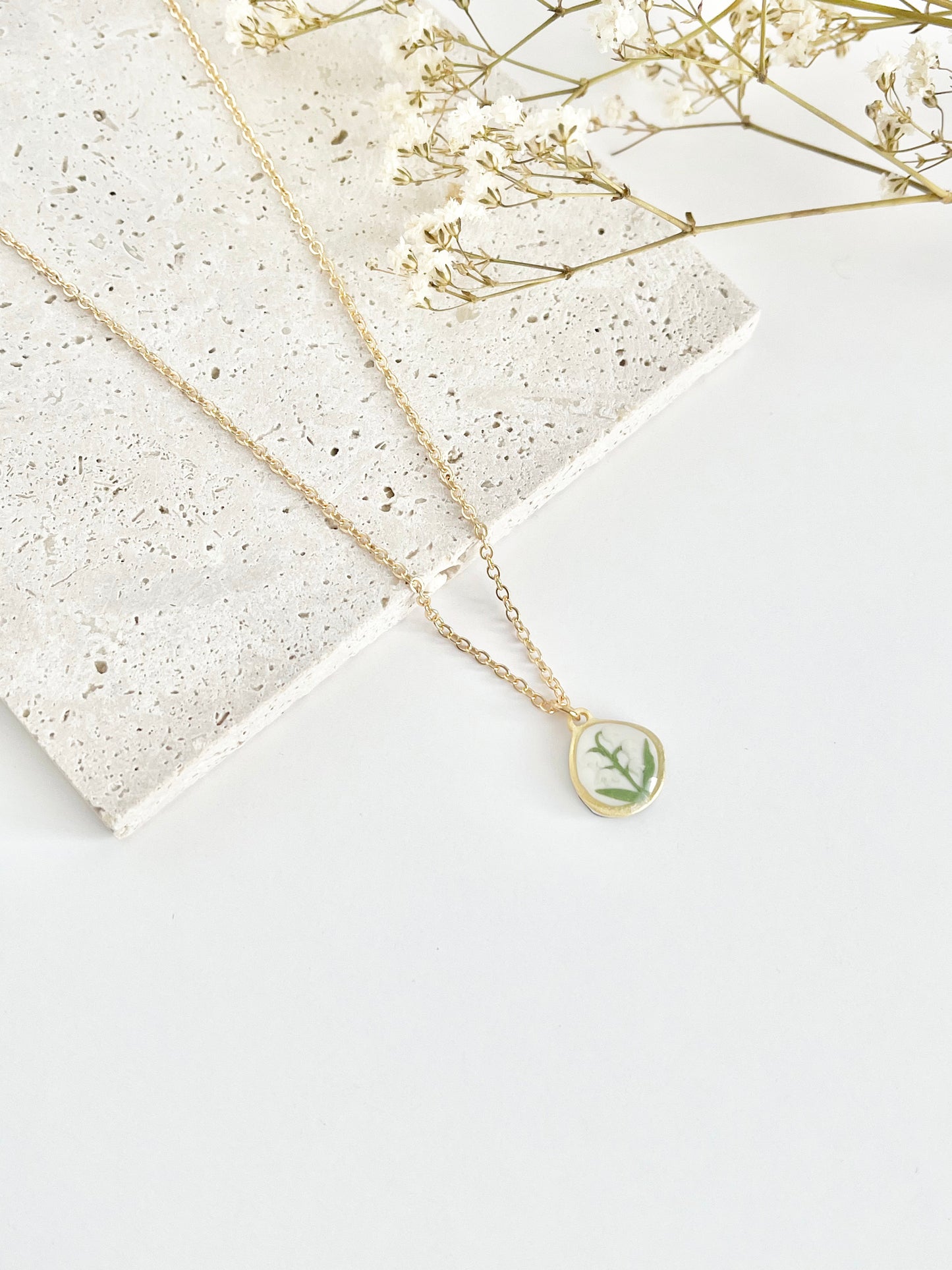 Gold clay necklace with a lily of the valley pendant on a white surface with dried flowers.