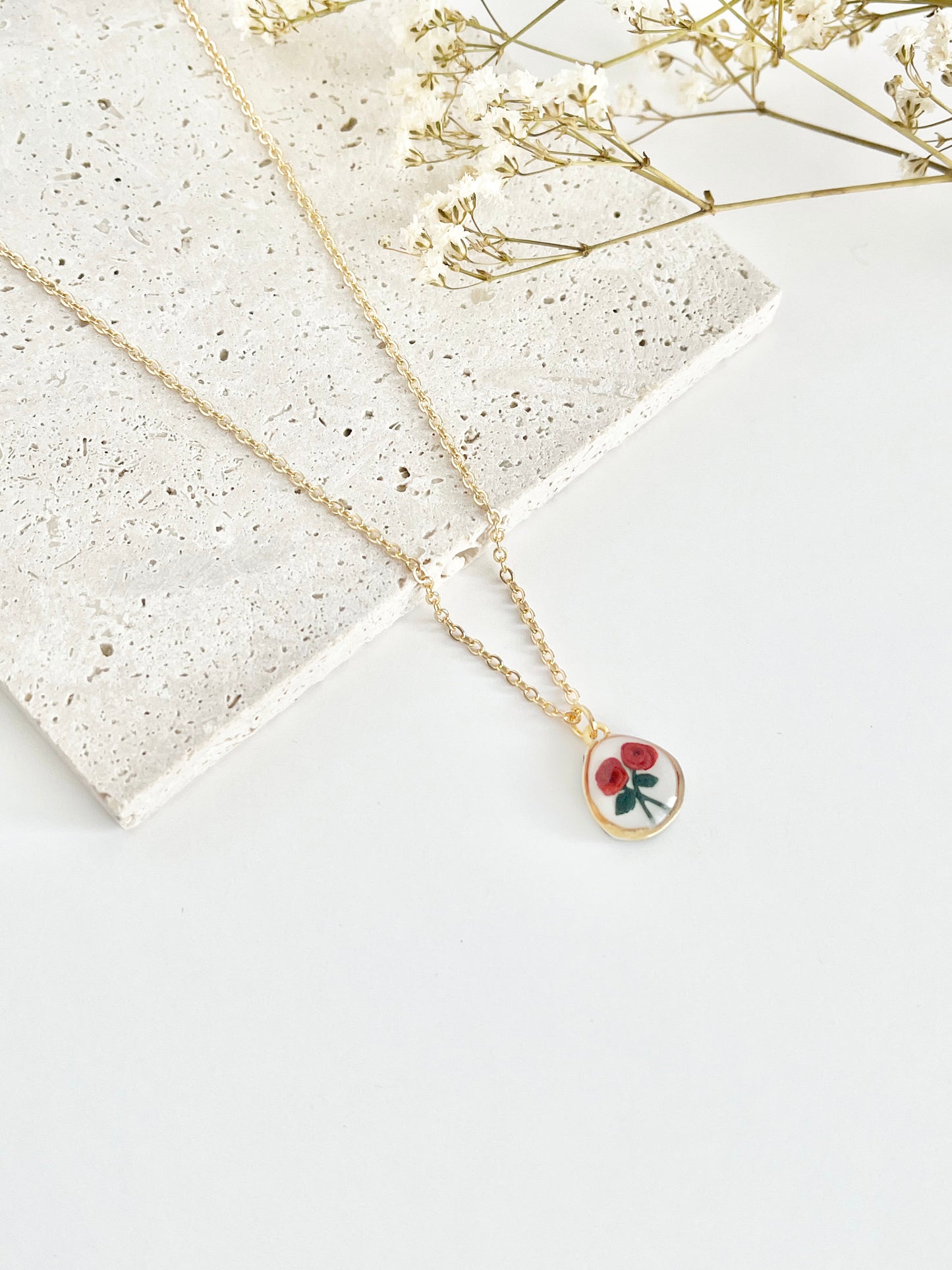 Gold clay necklace with a rose pendant on a light surface next to dried flowers