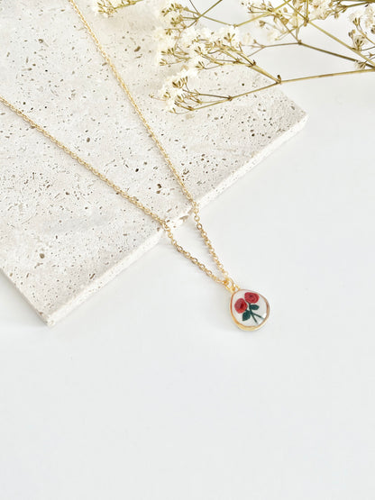 Gold clay necklace with a rose pendant on a light surface next to dried flowers
