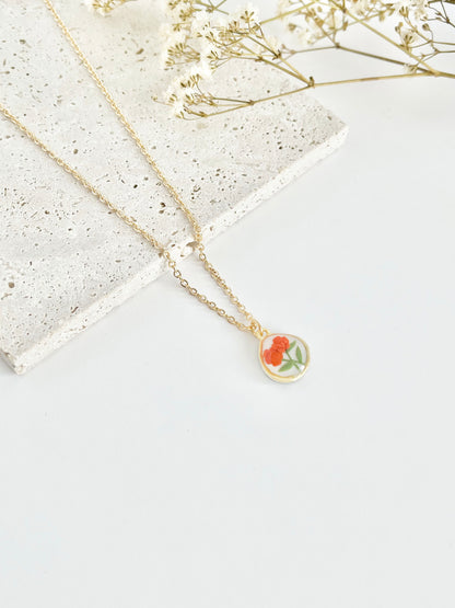 Gold clay necklace with a floral pendant on a light surface