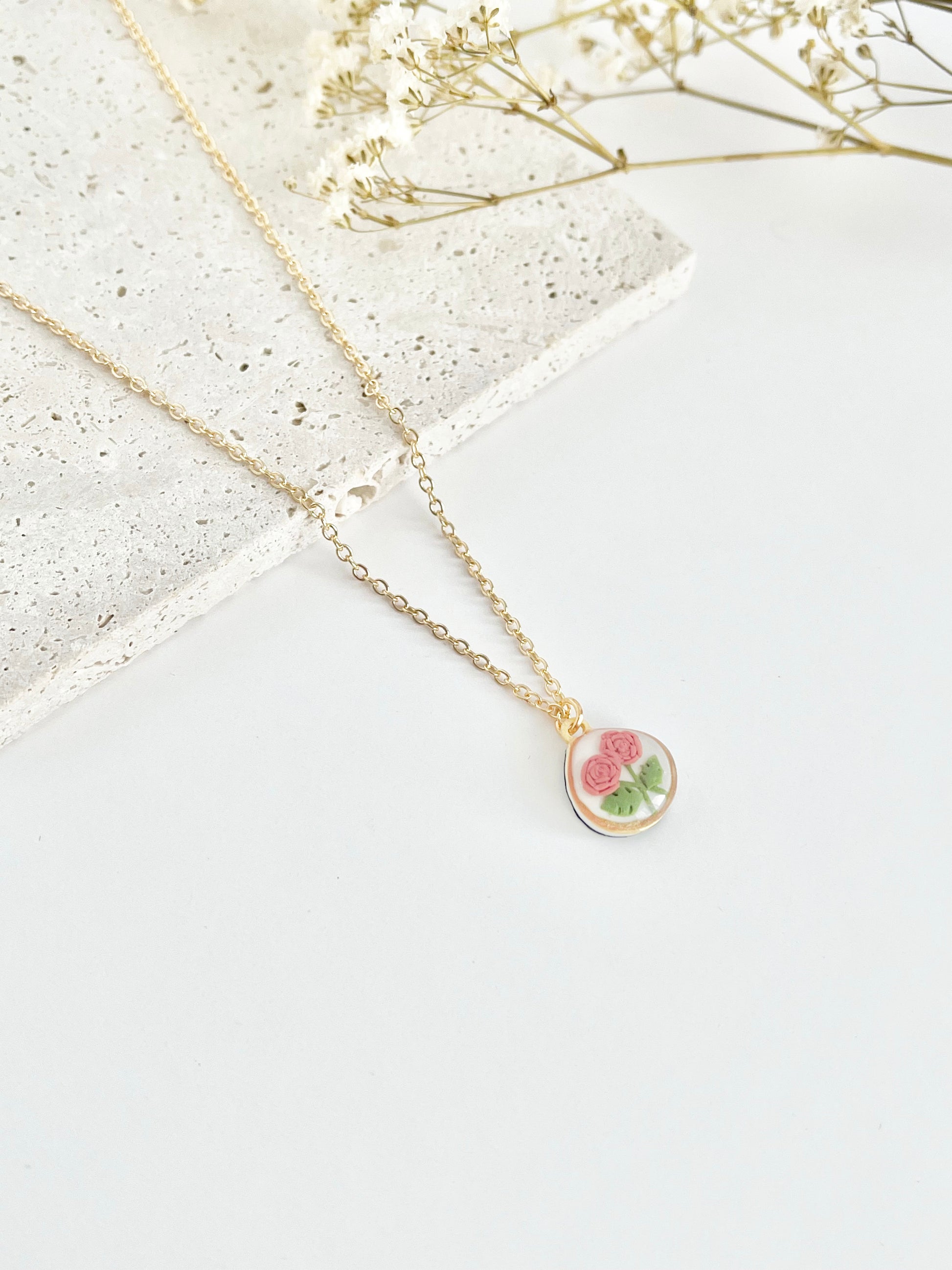 Gold clay necklace with a floral pendant on a light surface