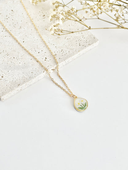 Gold clay necklace with a floral pendant on a light surface with dried flowers.