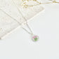 A silver clay necklace with a small carnation pendant laid on a flat white surface next to dried flowers