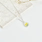 Silver clay necklace with a small daffodil pendant on a white surface with dried flowers.
