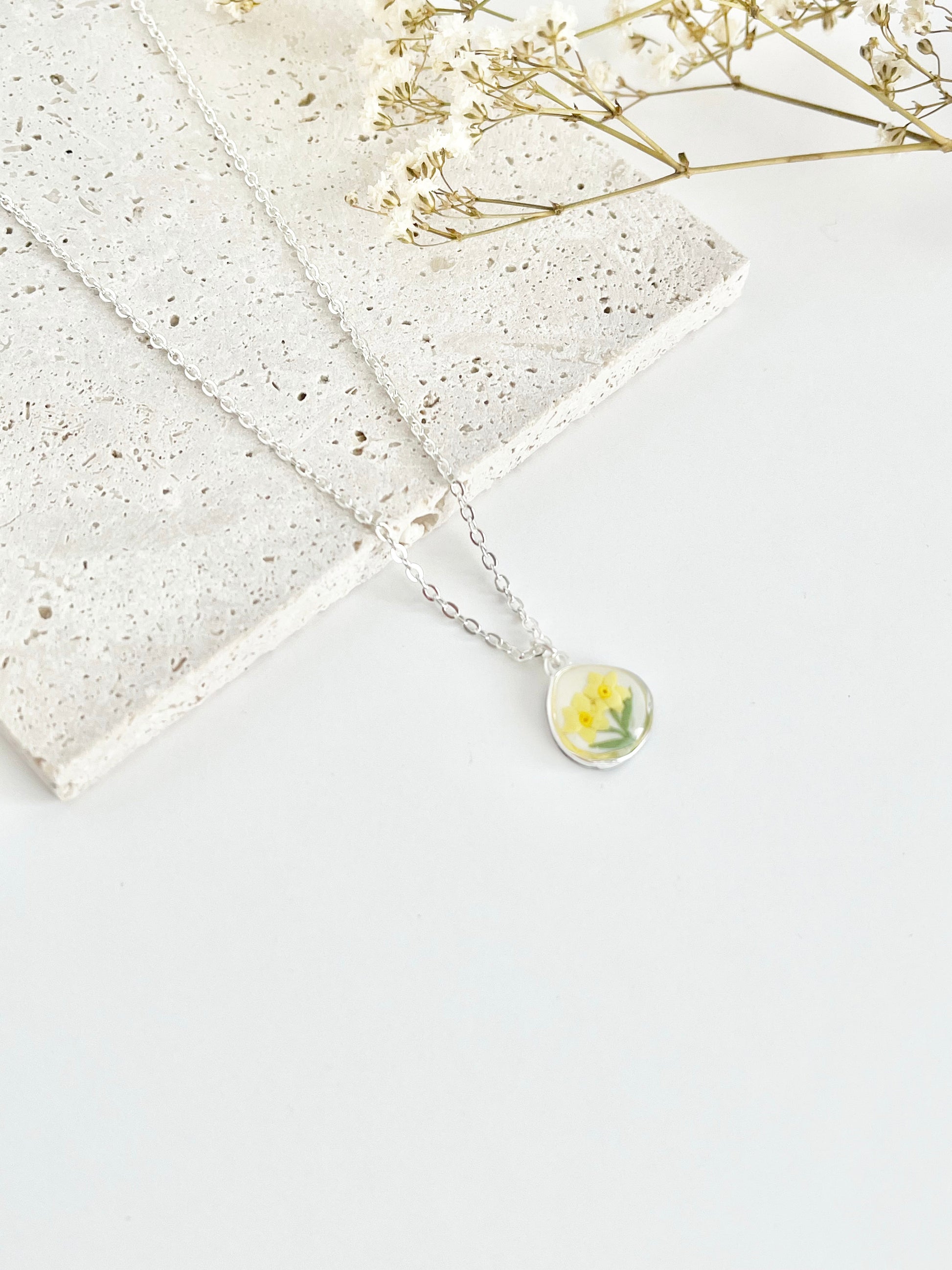Silver clay necklace with a small daffodil pendant on a white surface with dried flowers.