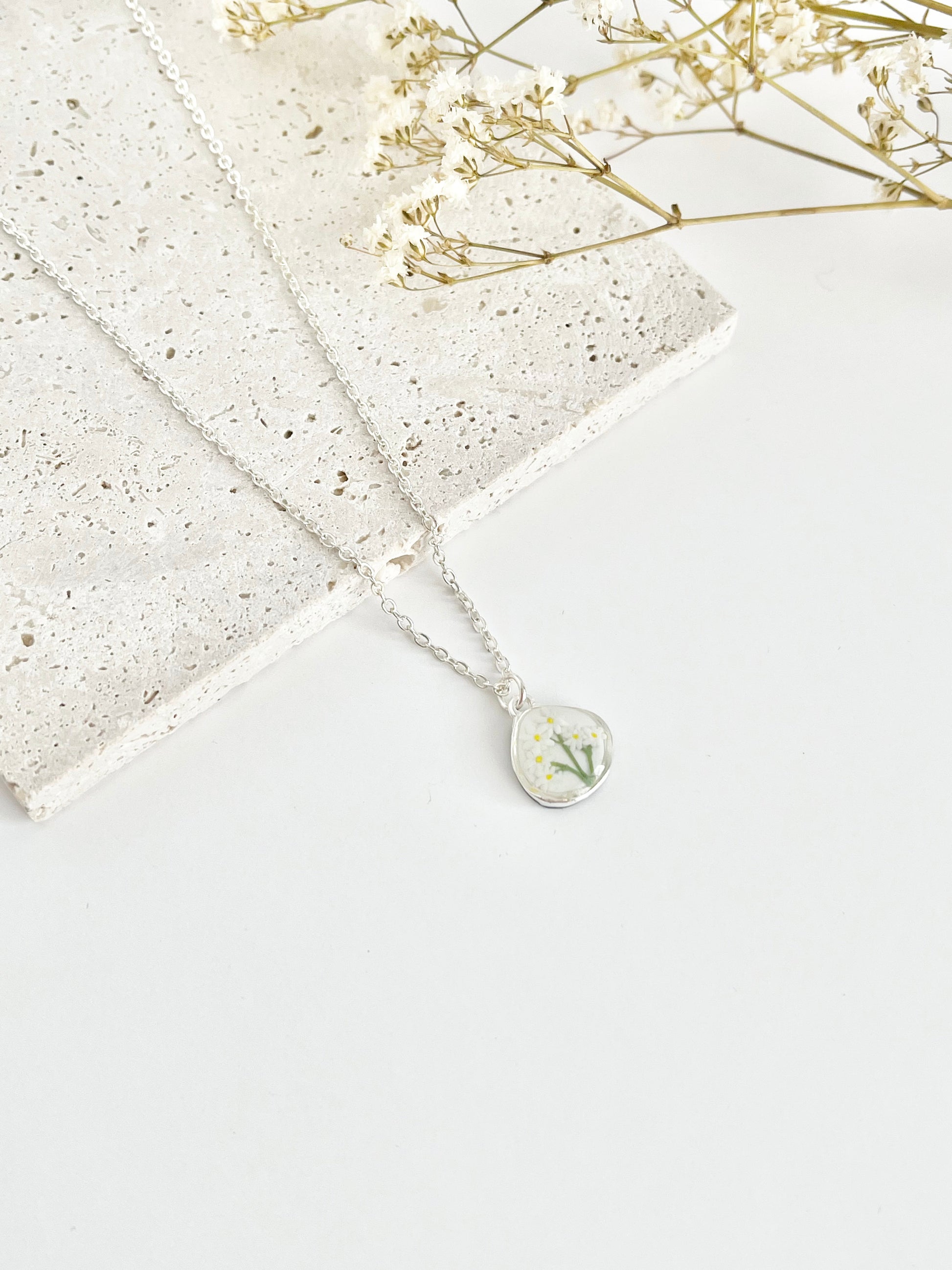 silver necklace with a small daisy pendant on a textured surface with dried flowers