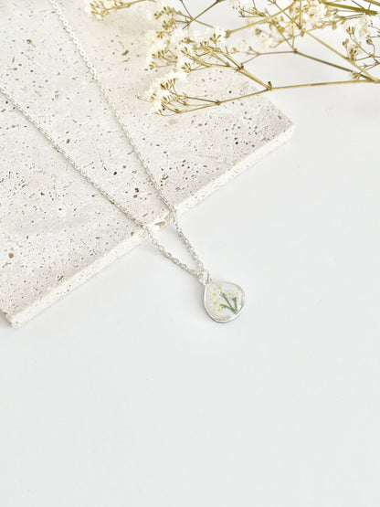 silver clay necklace with a small daisy pendant on a textured surface with dried flowers