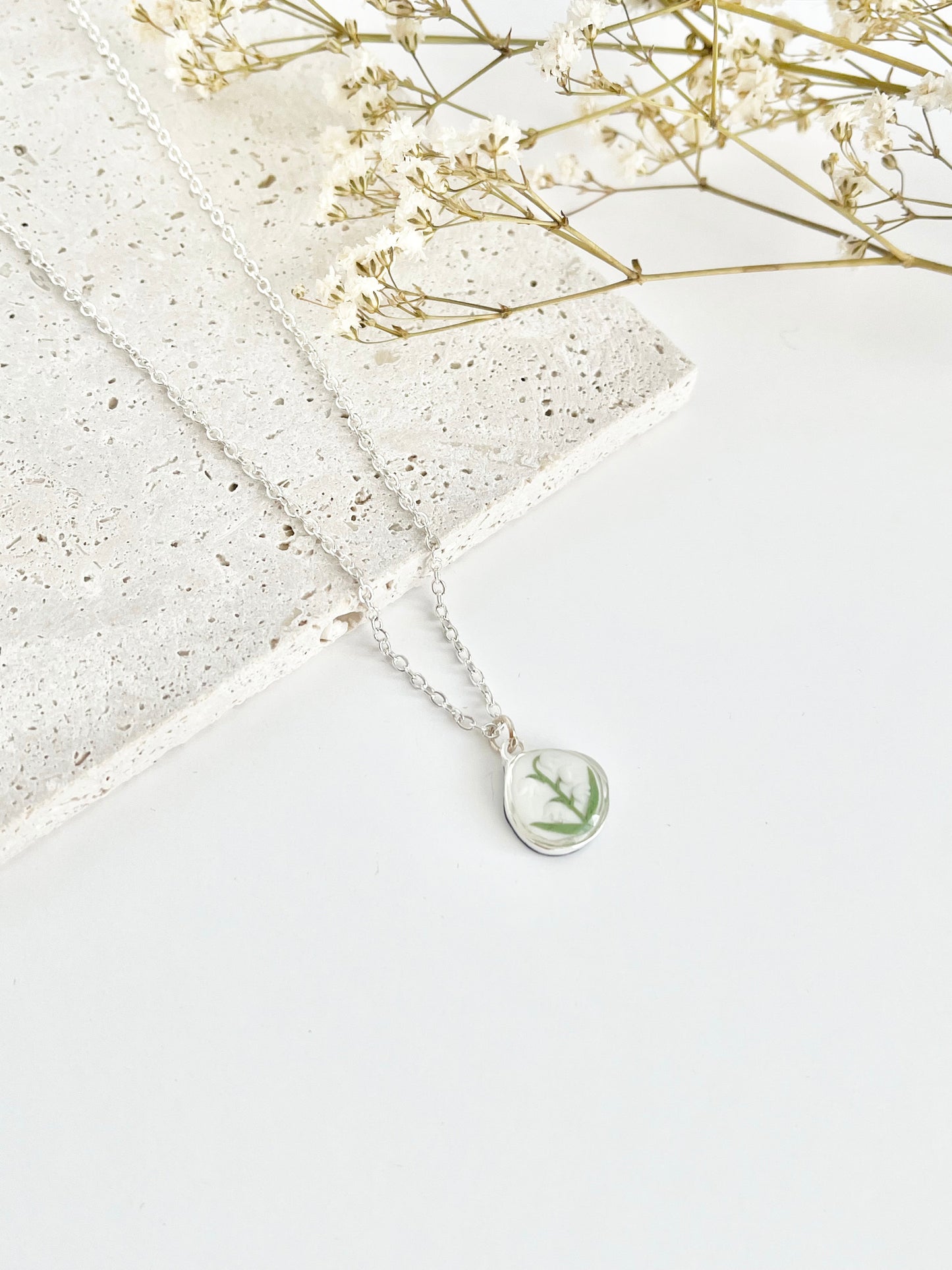 Silver clay necklace with a lily of the valley pendant on a white surface with dried flowers.