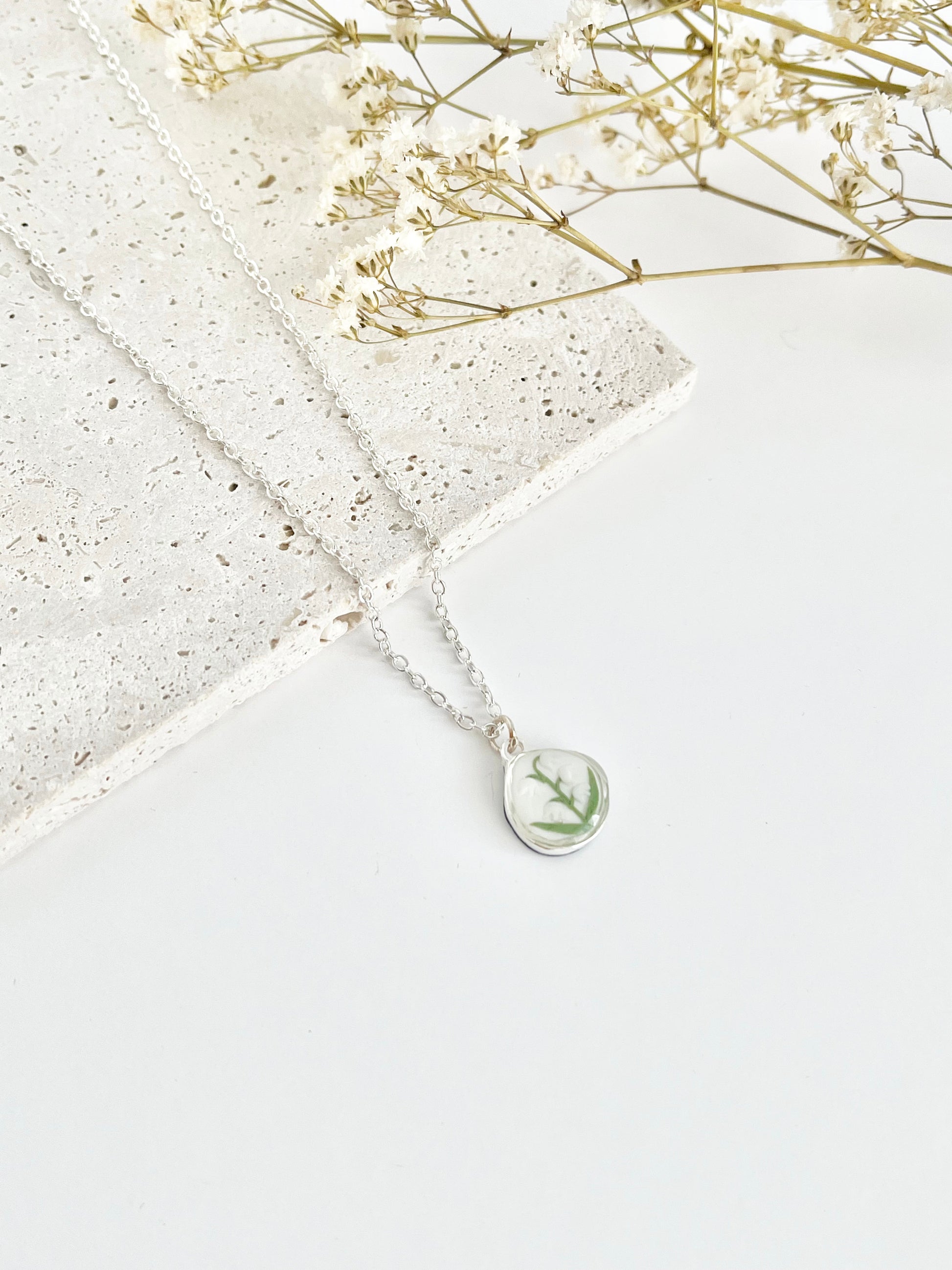 Silver clay necklace with a lily of the valley pendant on a white surface with dried flowers.