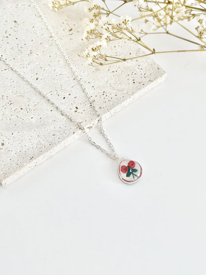 Silver clay necklace with a rose pendant on a light surface next to dried flowers