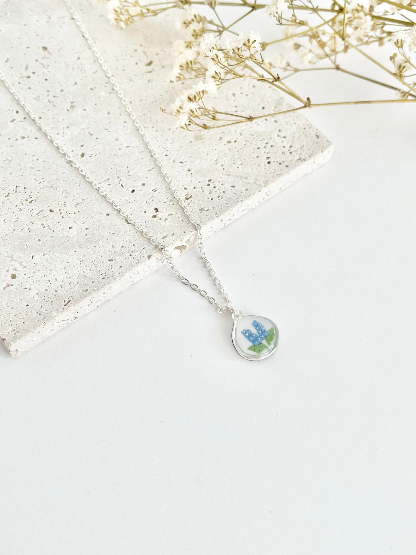 Silver clay necklace with a pendant featuring a floral design on a light background