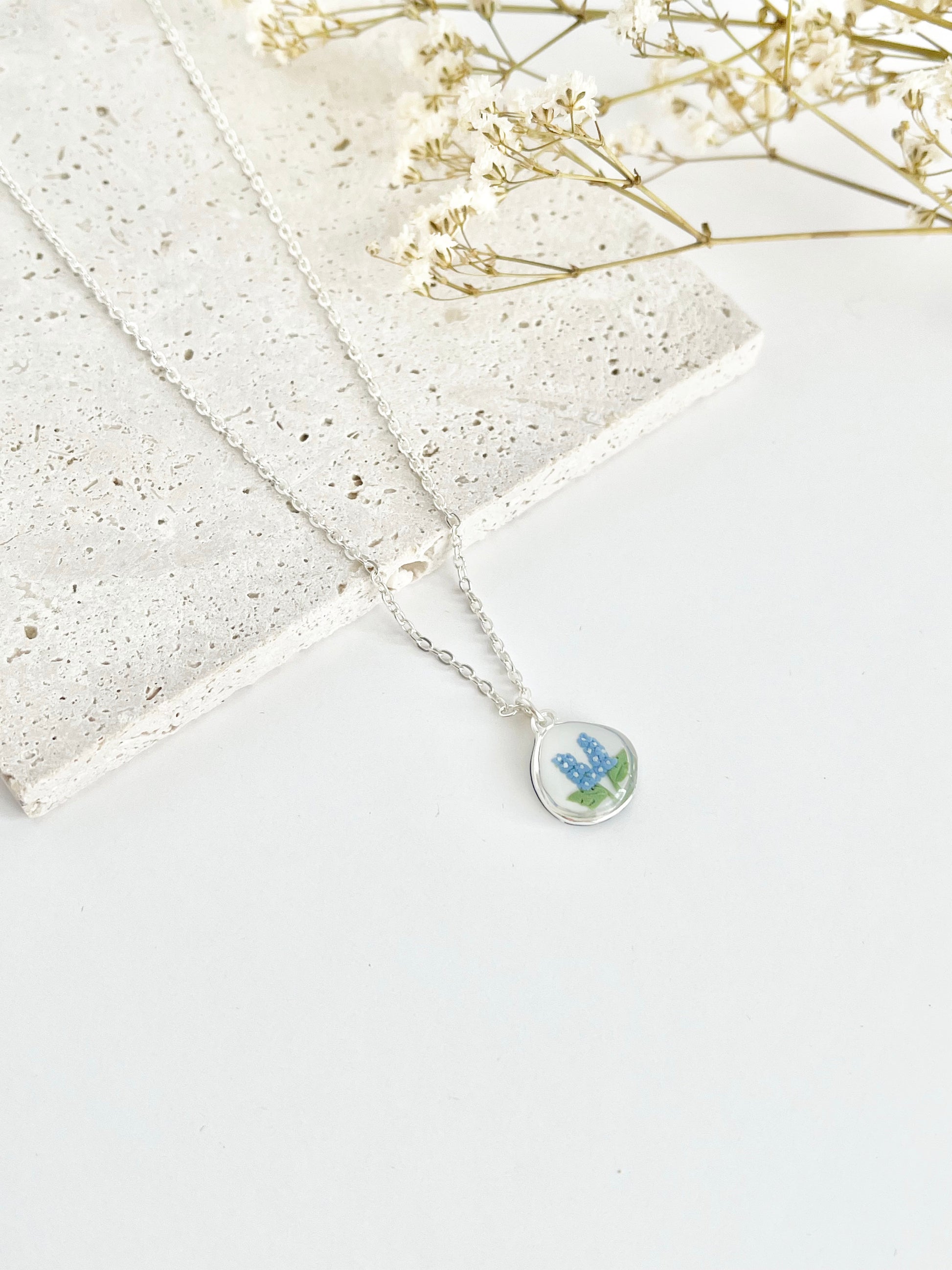 Silver clay necklace with a pendant featuring a floral design on a light background