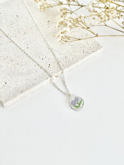 Silver clay necklace with a floral pendant on a light background next to dried flowers