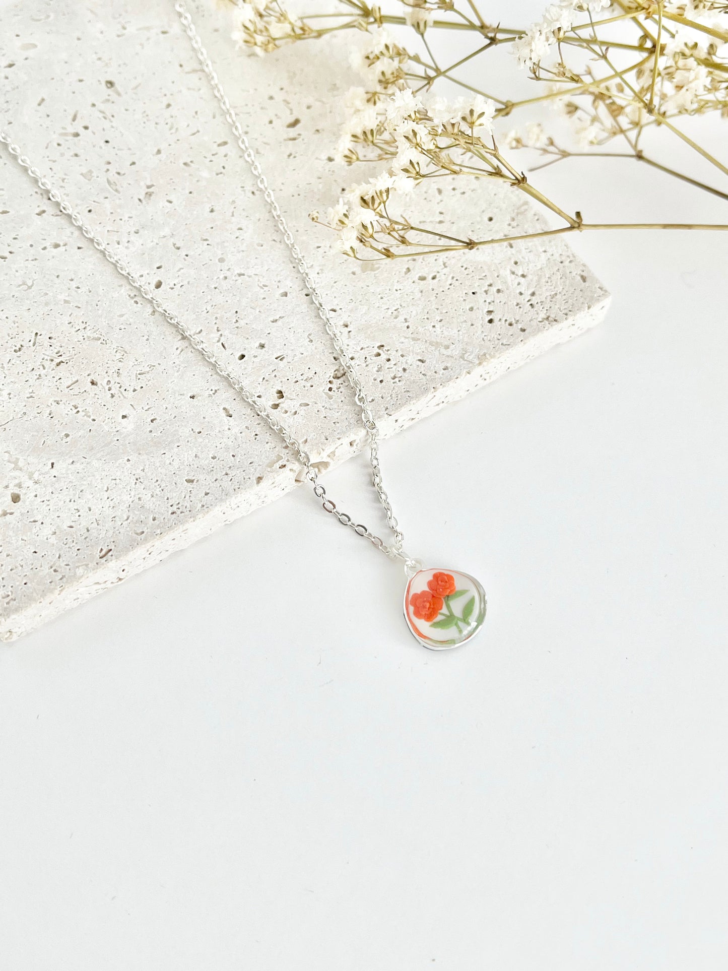 Silver clay necklace with a floral pendant on a light surface