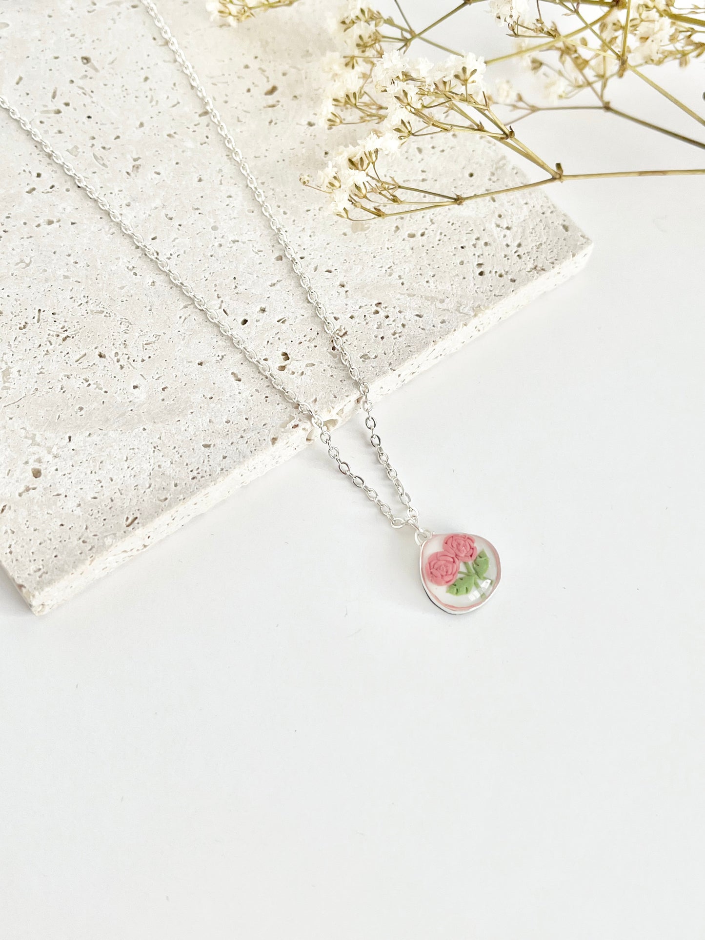 Silver clay necklace with a floral pendant on a light surface