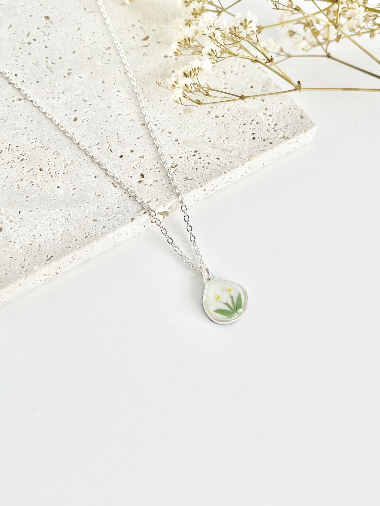 Silver clay necklace with a floral pendant on a light surface with dried flowers.