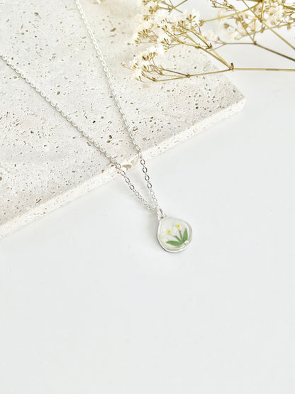 Silver clay necklace with a floral pendant on a light surface with dried flowers.