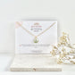 Gold clay necklace with a lily of the valley pendant on a jewellery card on top of a textured tile, with dried flowers beside it.