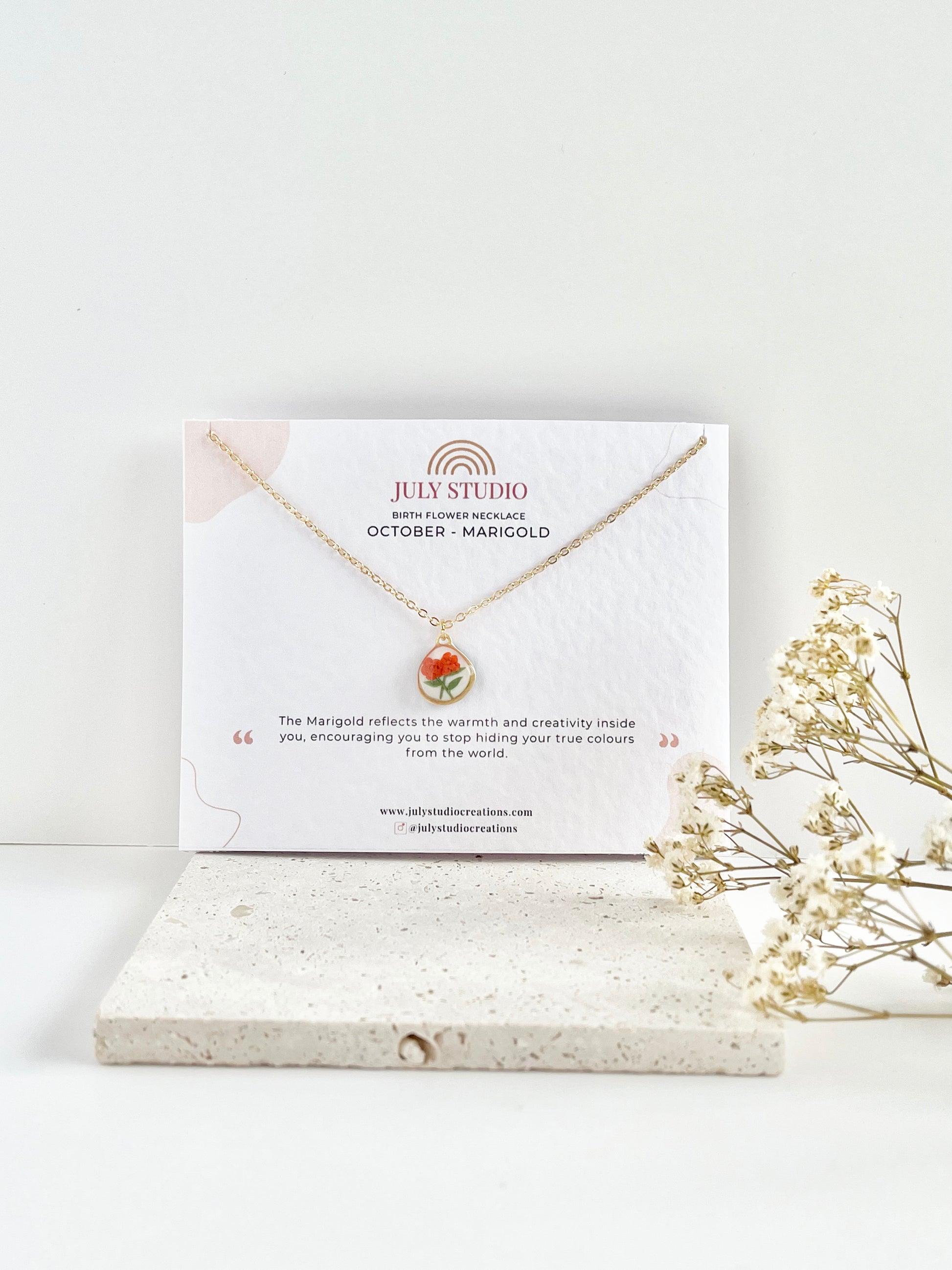 Gold clay necklace with a floral pendant on a July Studio jewellery card with a white background