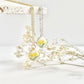 Gold necklace and silver clay necklace with daffodil pendant hanging from a tile against a white background with dried flowers in the background