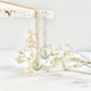 A gold and silver clay necklace with teardrop pendants hanging from a textured tile and dried flowers in the background